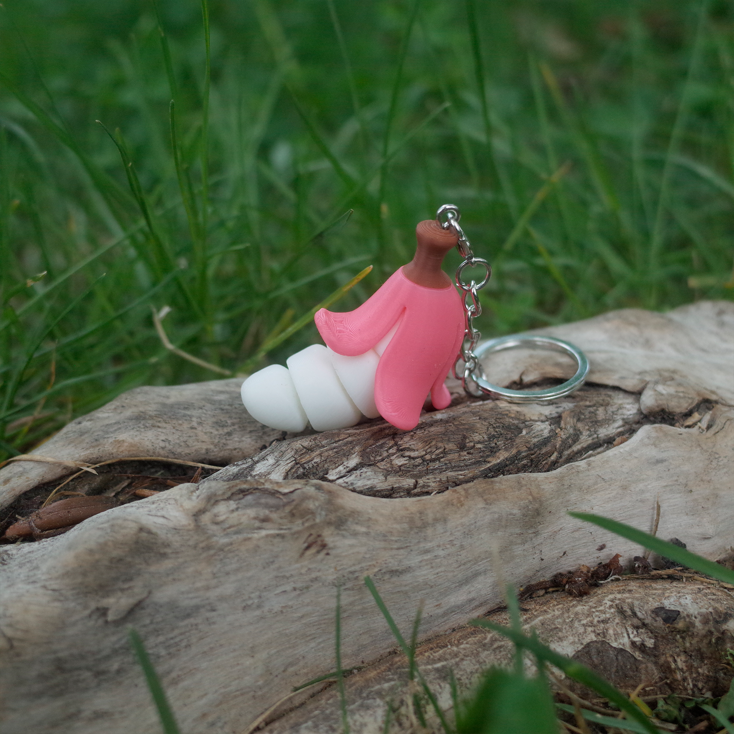 A pink peeled chubby banana keychain laying sideways on wood, featuring a curly white banana body.