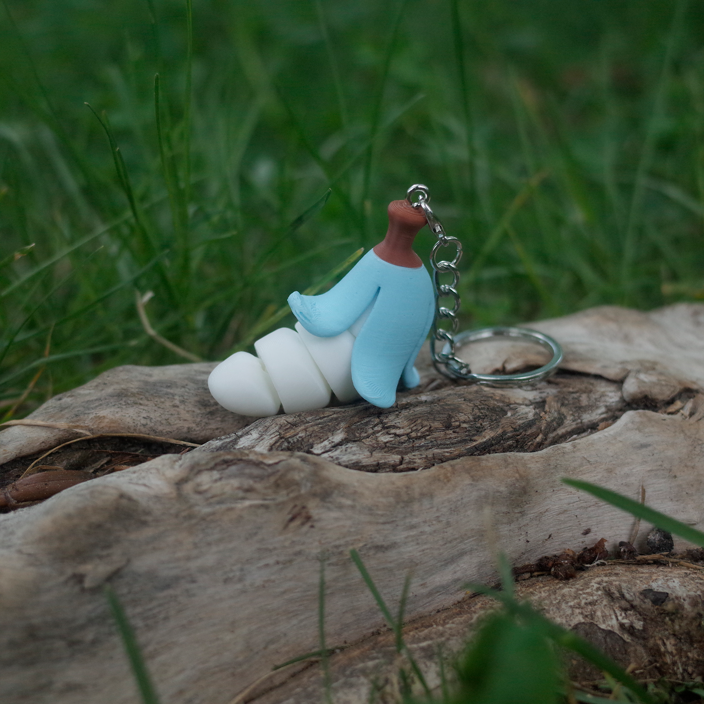 A chubby banana charm featuring a pastel blue peel and soft white body, displayed outdoors on a log.