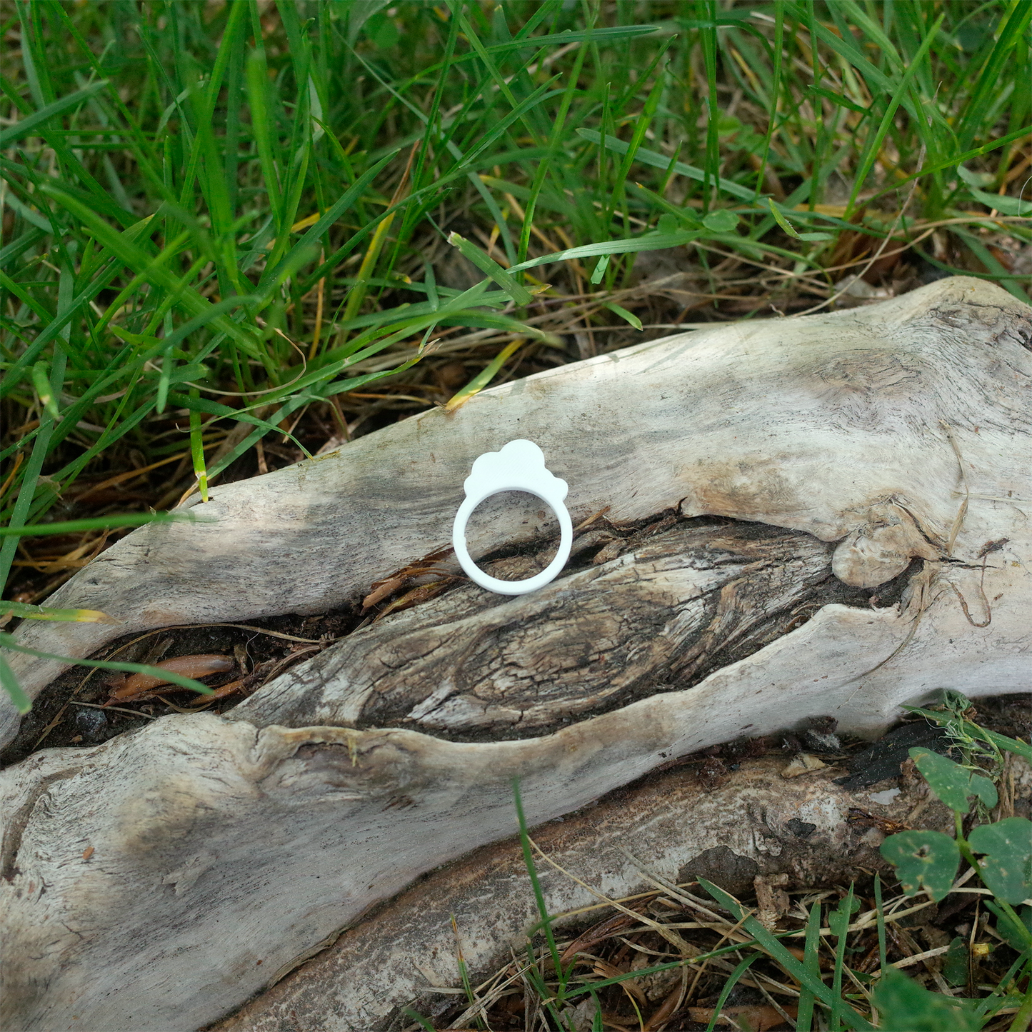 A white 3D printed ring shaped like a simple fluffy cloud, placed on a natural tree background.