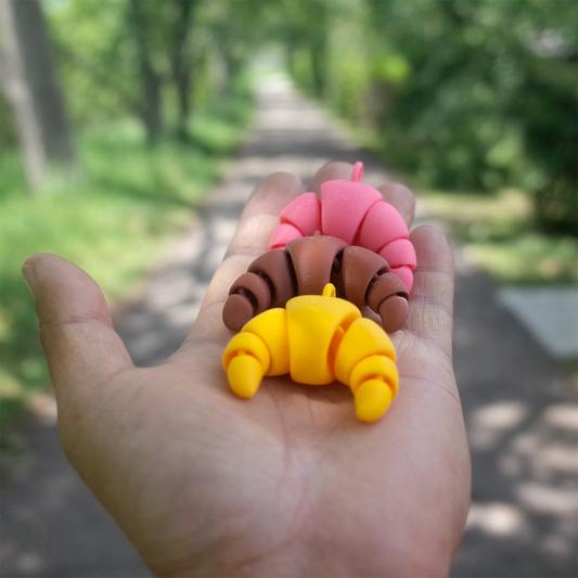 3D printed croissants in yellow, brown and pink PLA on a palm, perfect as a keychain and bagcharm – PrintBabe