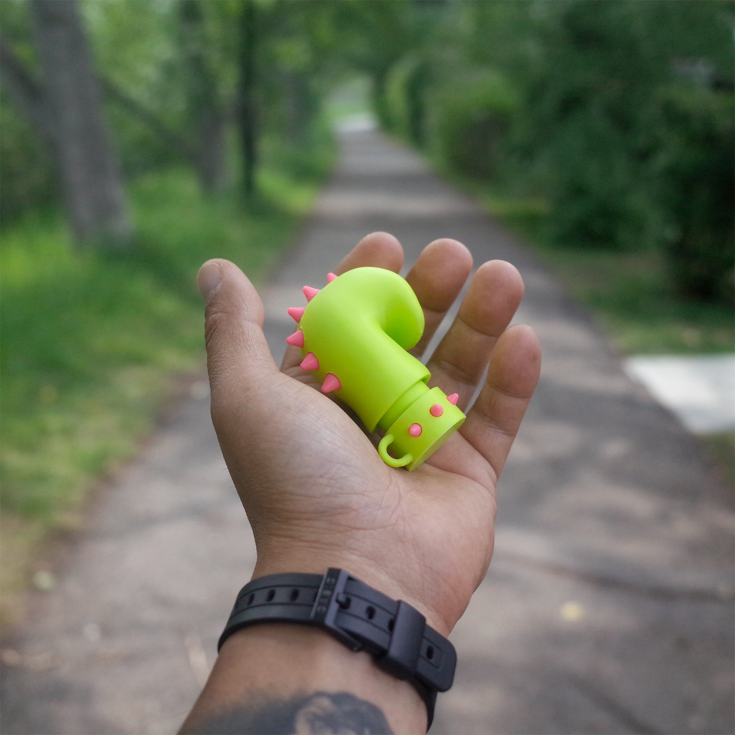 Bright green spiked glove charm held in hand on a tree-lined path
