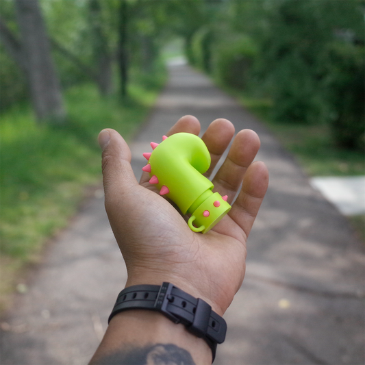 Bright green spiked glove charm held in hand on a tree-lined path