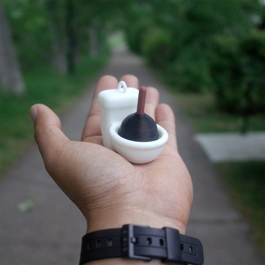 Person holding a tiny 3D printed toilet toy with plunger in hand