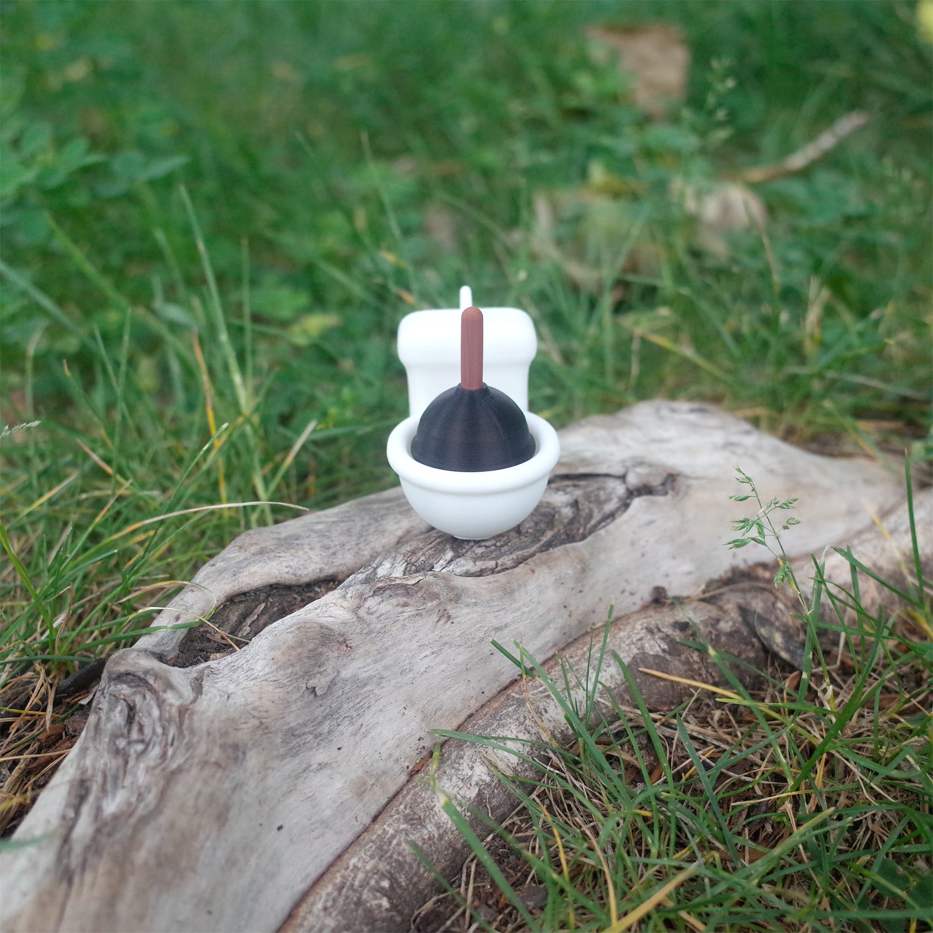 Stucky Toilet resting on tree bark, surrounded by green grass