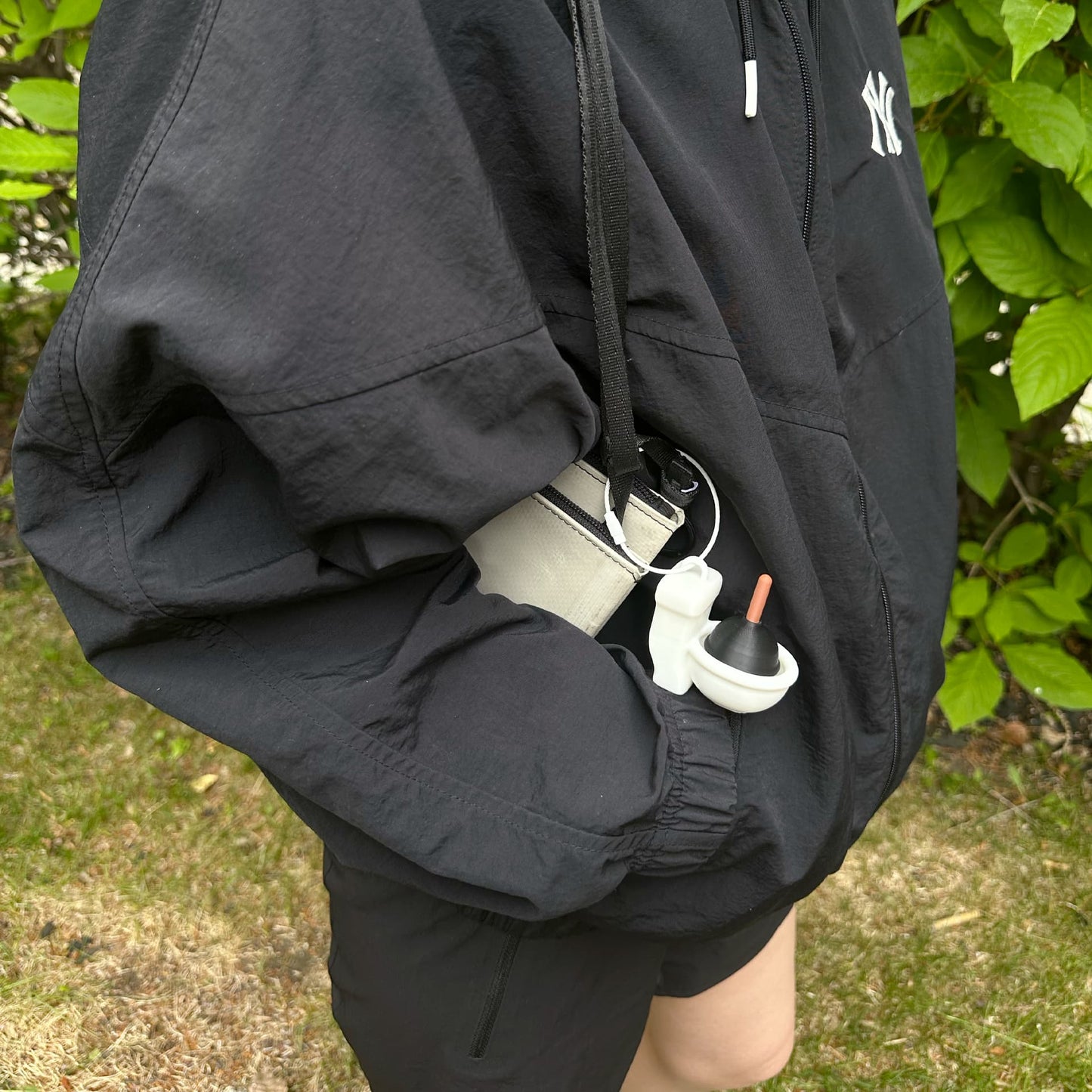 Mini toilet charm dangling from a strap on black jacket outdoors