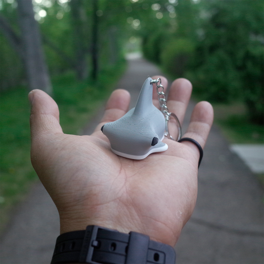 A hand holding the gray hammerhead shark 3D printed keychain, showcasing the smooth curves and classic silhouette of the fish.