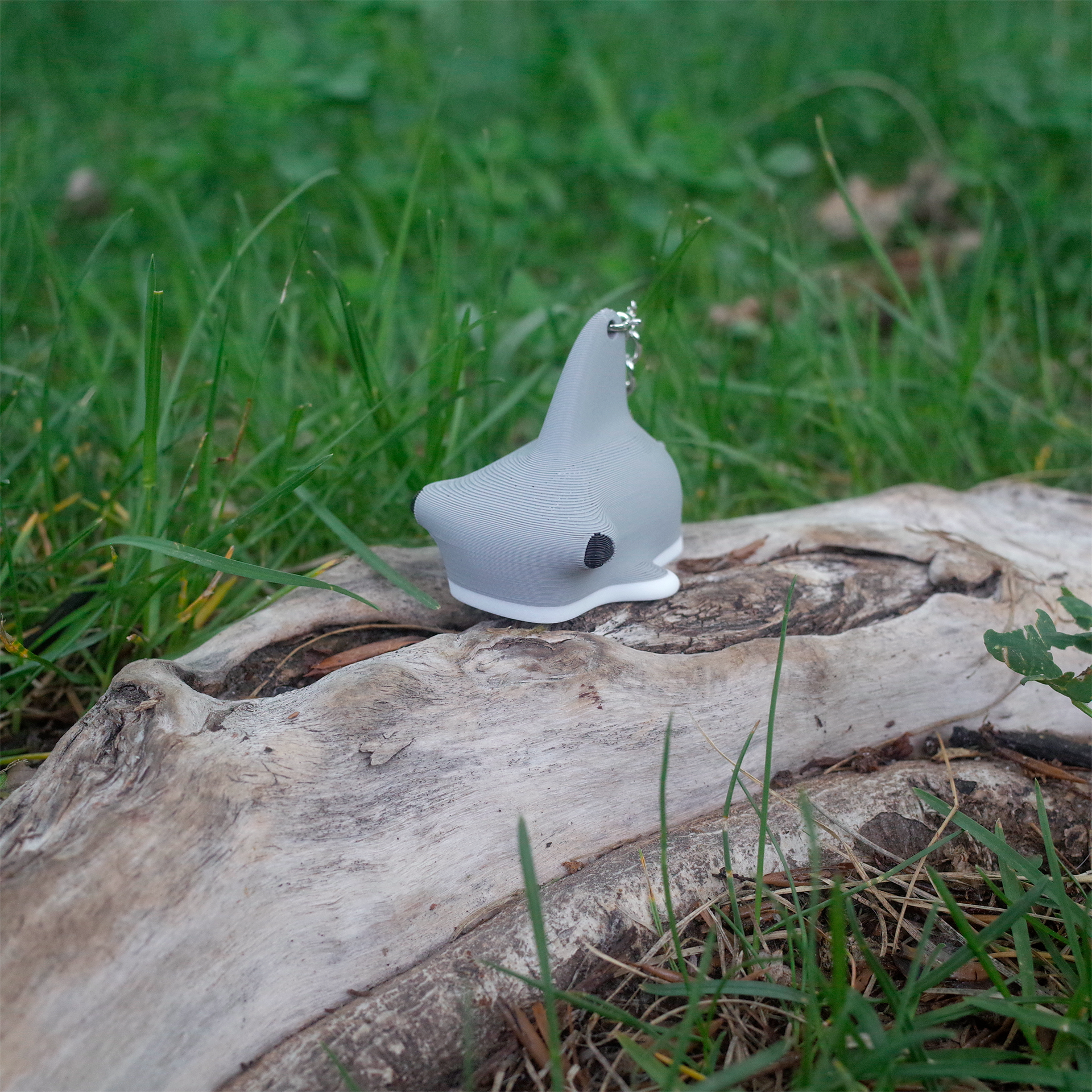 Gray hammerhead shark 3D printed charm, viewed from the front side with its wide head and small black eye visible, placed on wood.