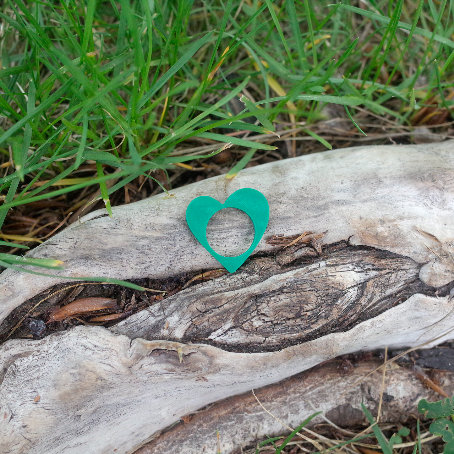 A vivid green heart-shaped 3D printed ring resting on a rustic log.