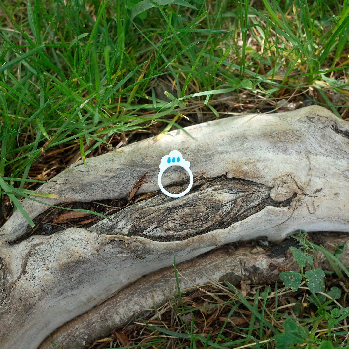 A white ring with blue raindrops above a cloud, 3D printed and displayed outdoors on bark.