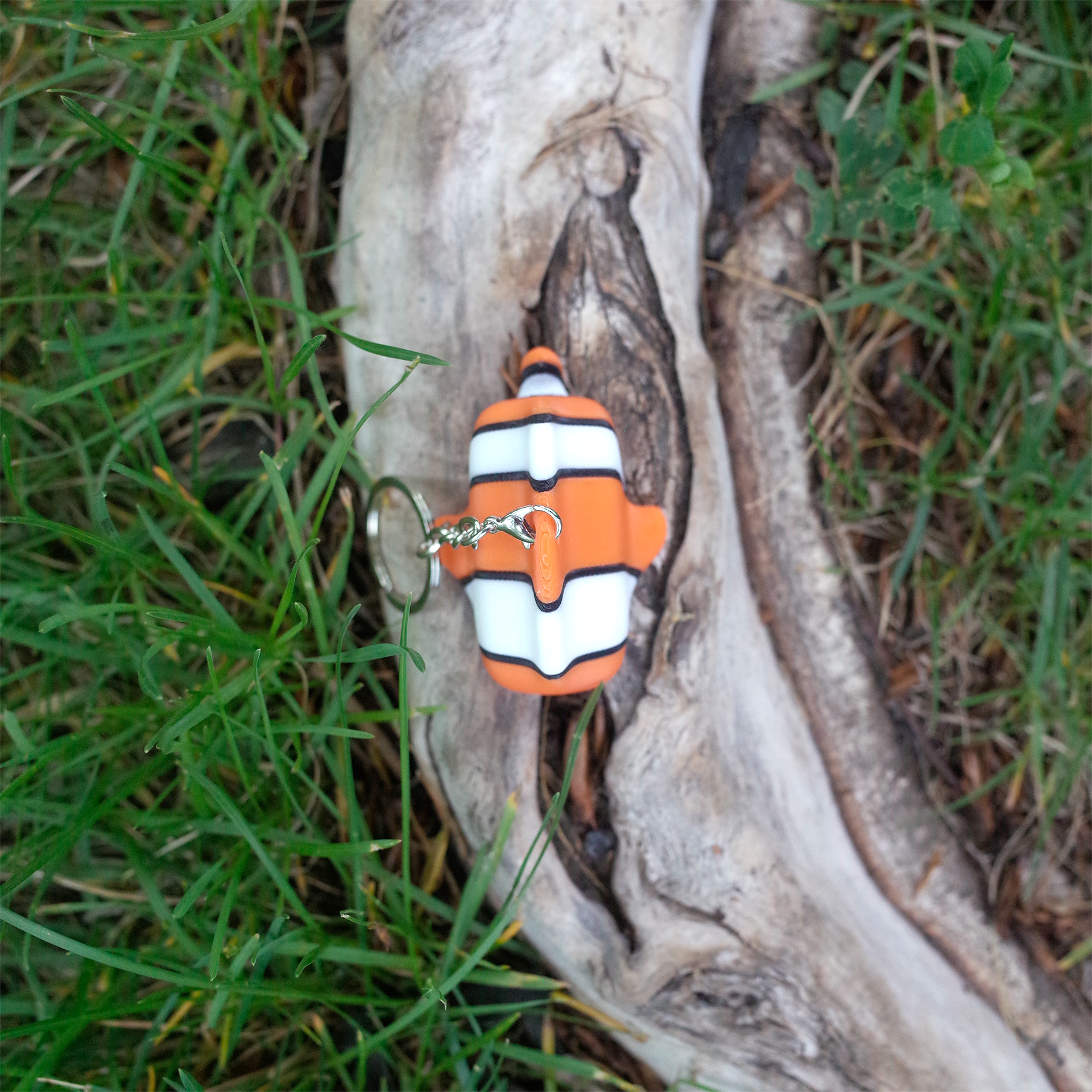 Top-down view of a 3D printed clownfish keychain lying on wood, showing the fin and body stripes clearly.