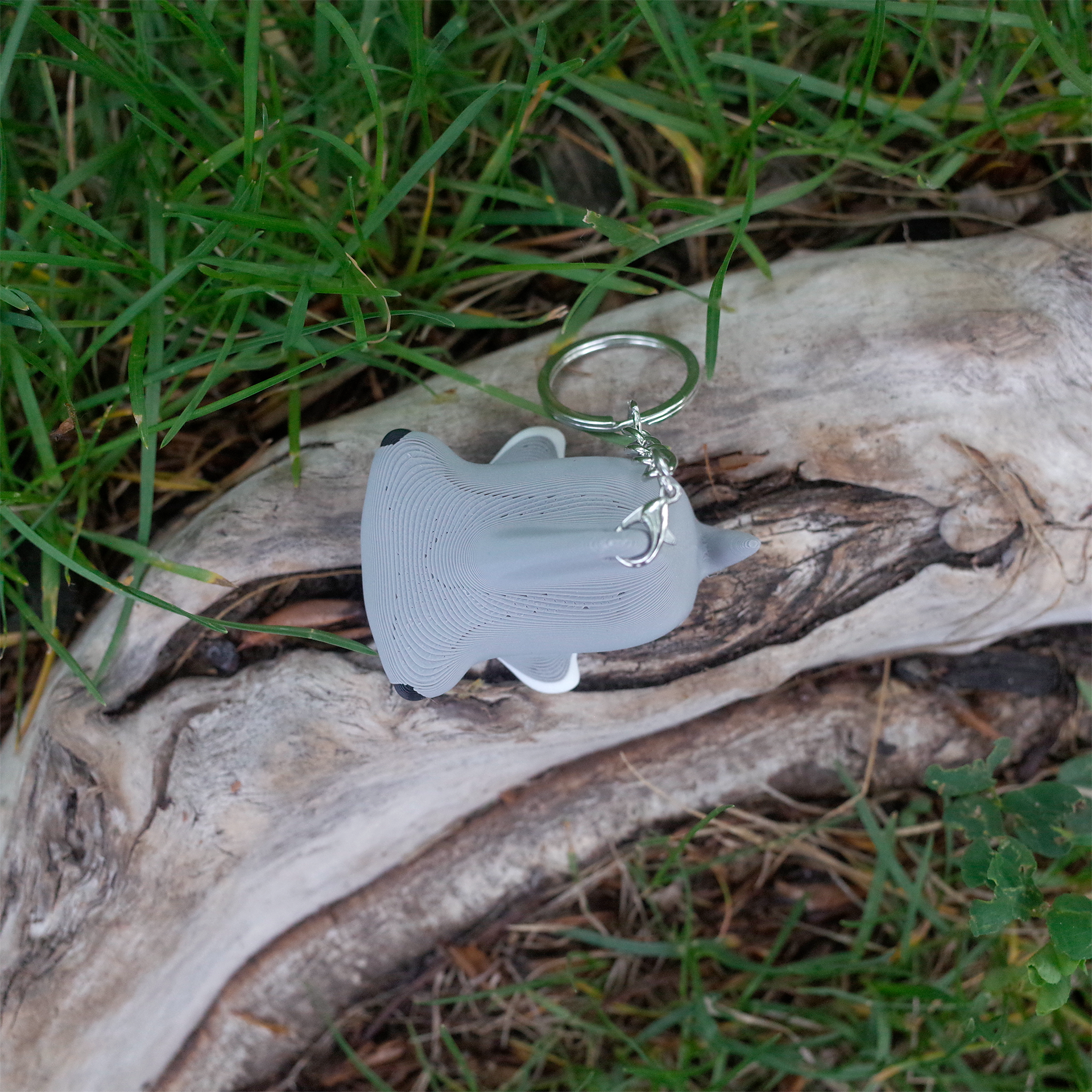 Gray hammerhead shark 3D printed charm, viewed from the front side with its wide head and small black eye visible, placed on wood.