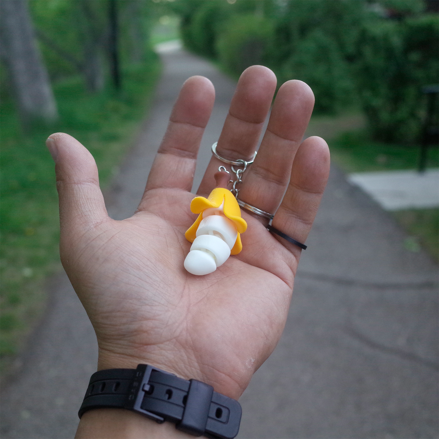 Hand holding a yellow Chubby Bananaz keychain with a coiled banana body, viewed from above outdoors.