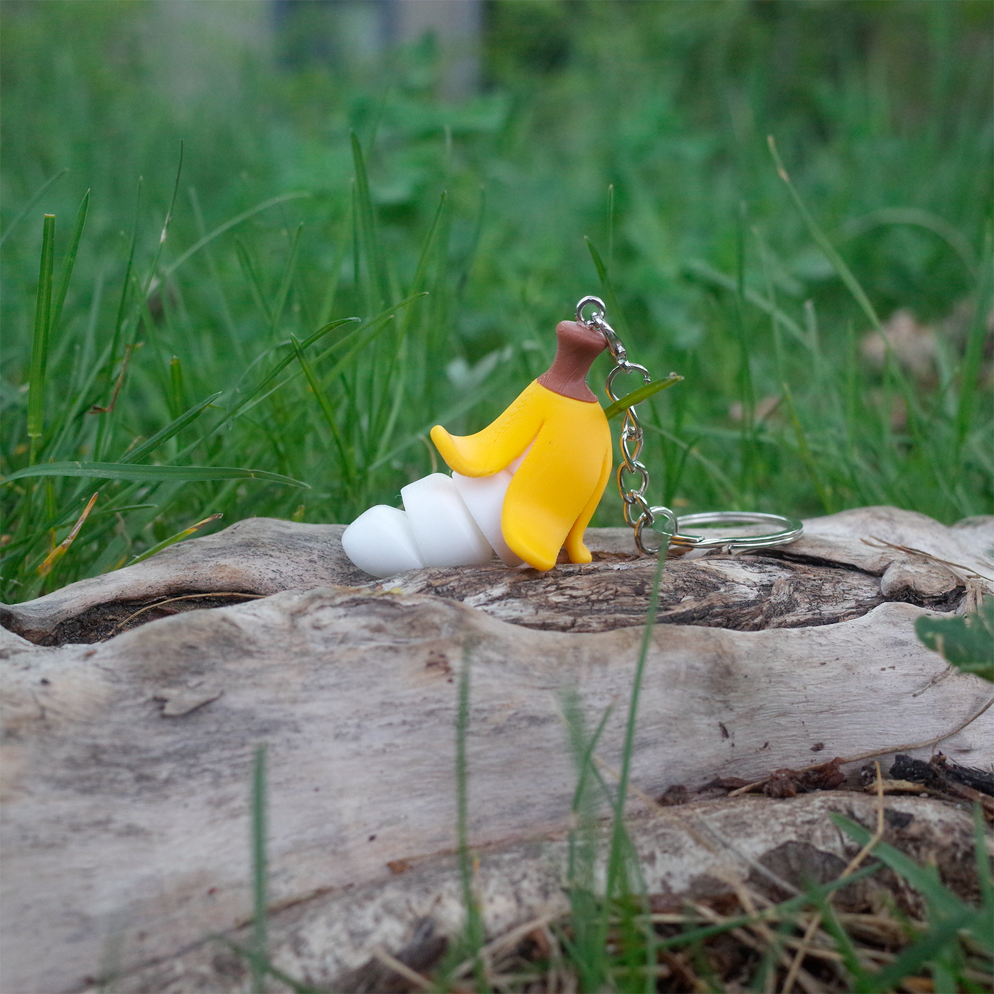 Yellow Chubby Bananaz keychain with a peeled top and spiral-shaped white banana, shown on wood in the grass.