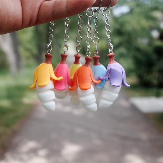 Hand holding up a full set of Chubby Bananaz 3D printed keychains, showing their colorful peels hanging in the air.