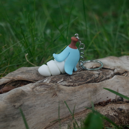 A chubby banana charm featuring a pastel blue peel and soft white body, displayed outdoors on a log.