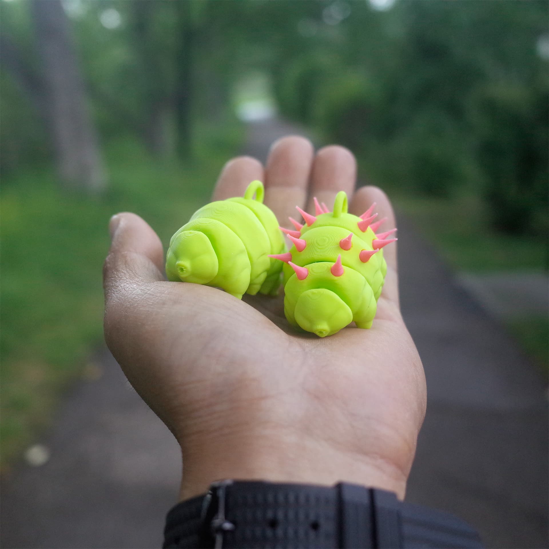 Two vivid green 3D printed tardigrades with punk details displayed in the palm of a hand.