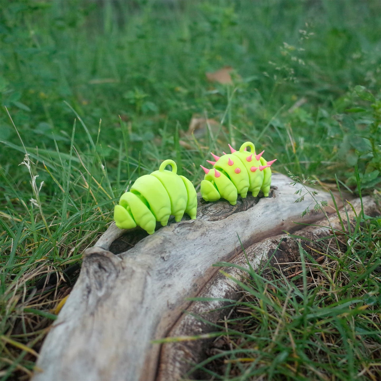 Two neon green 3D printed tardigrade charms side by side on driftwood—one plain and one with pink punk spikes.