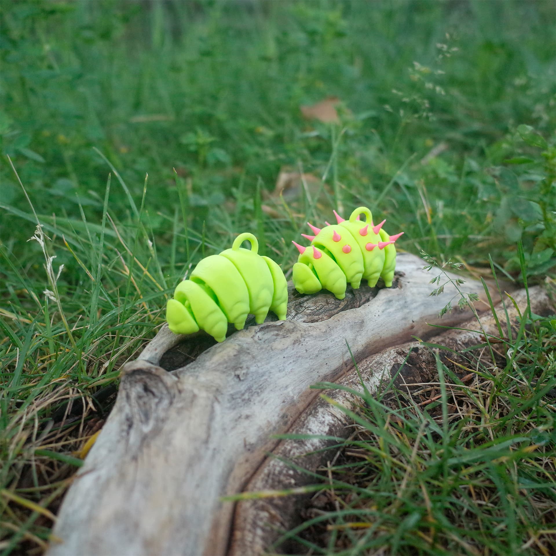 Two neon green 3D printed tardigrade charms side by side on driftwood—one plain and one with pink punk spikes.