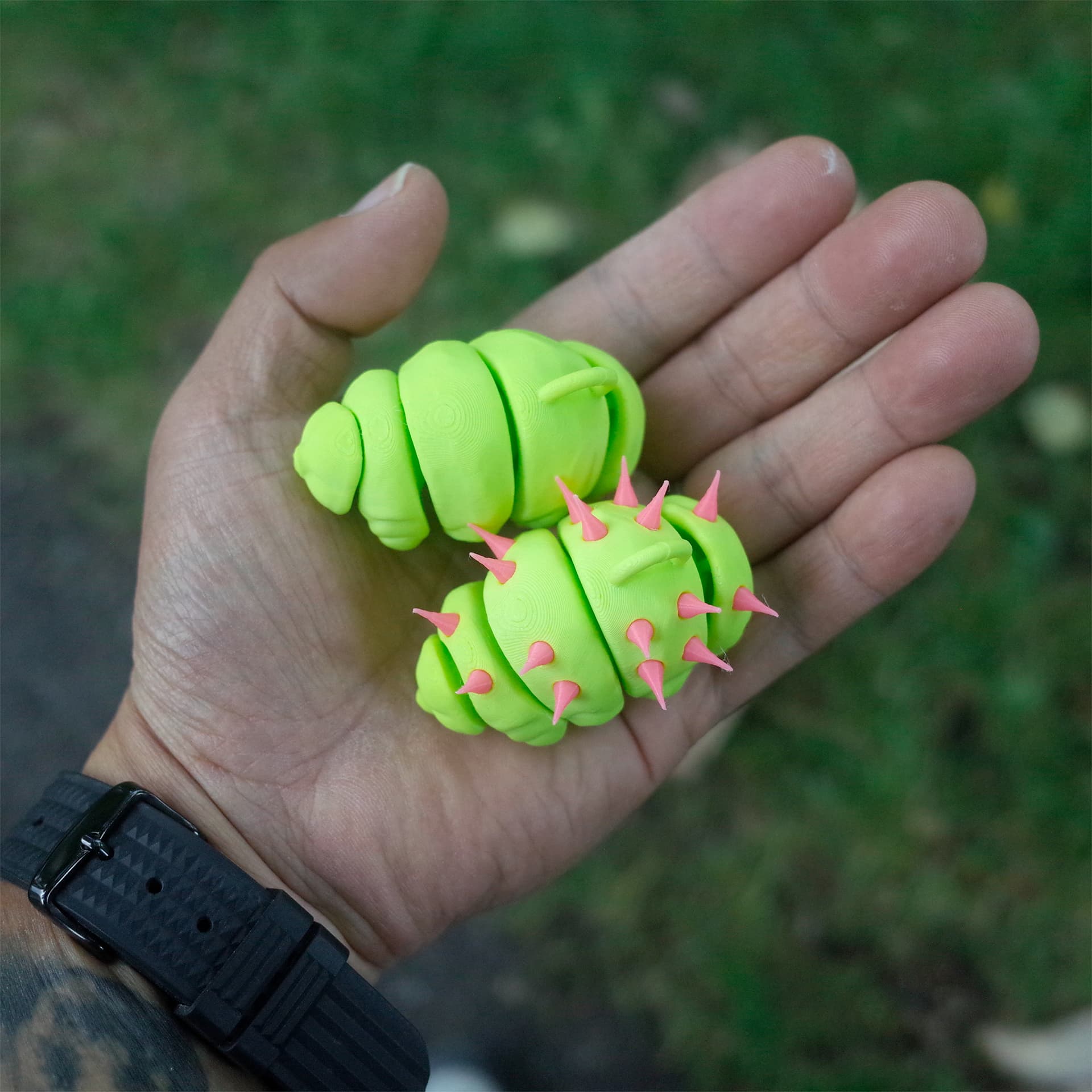 A close-up of a person's hand holding two 3D printed tardigrade toys - one smooth, one with pink spikes.