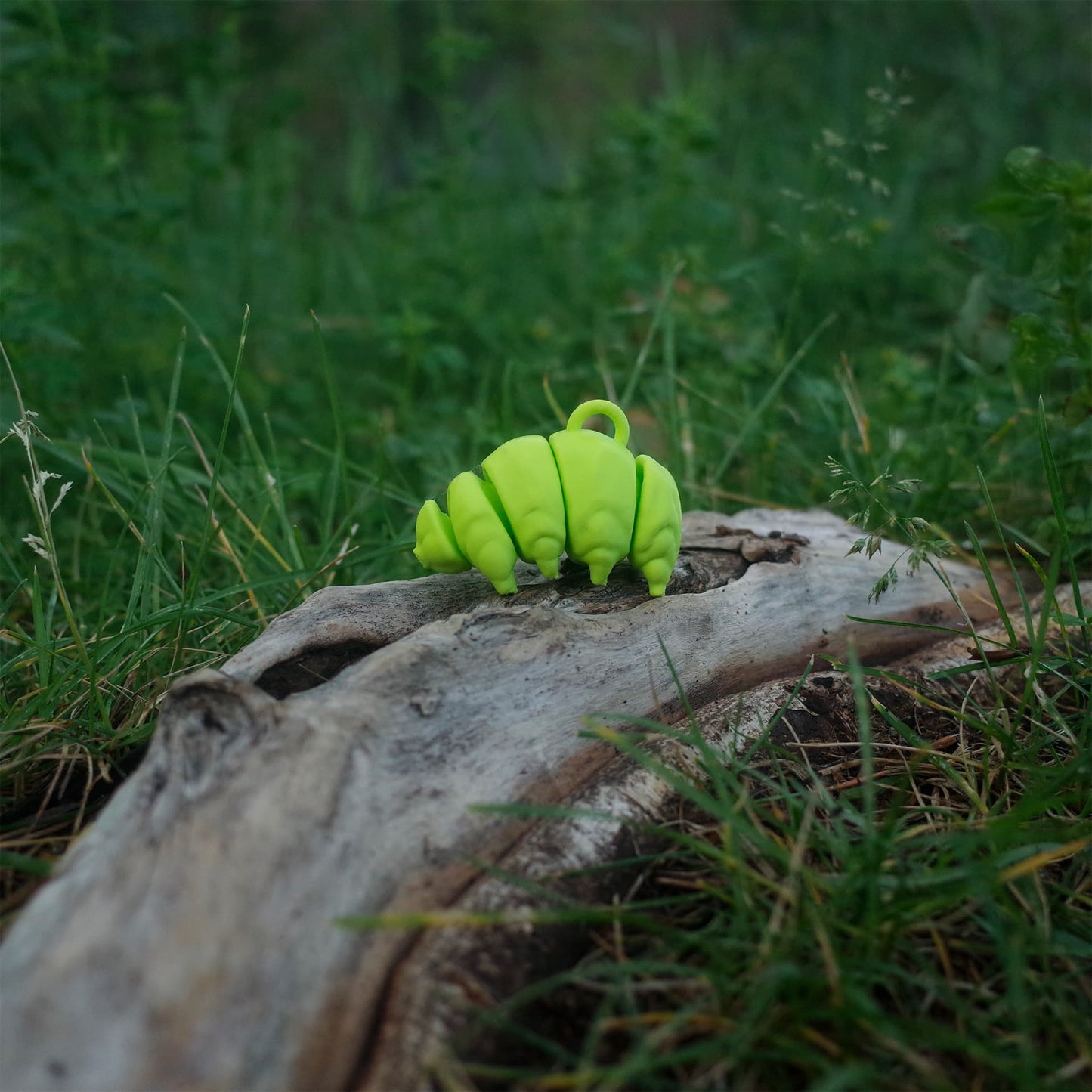 Side view of a smooth 3D printed green tardigrade figurine on driftwood in the grass.