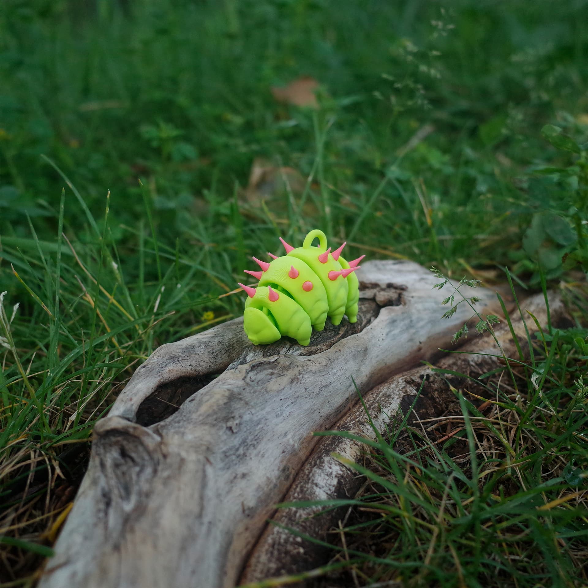 Quarter side view of a punk-style green tardigrade charm with hot pink spikes, posed on natural wood.