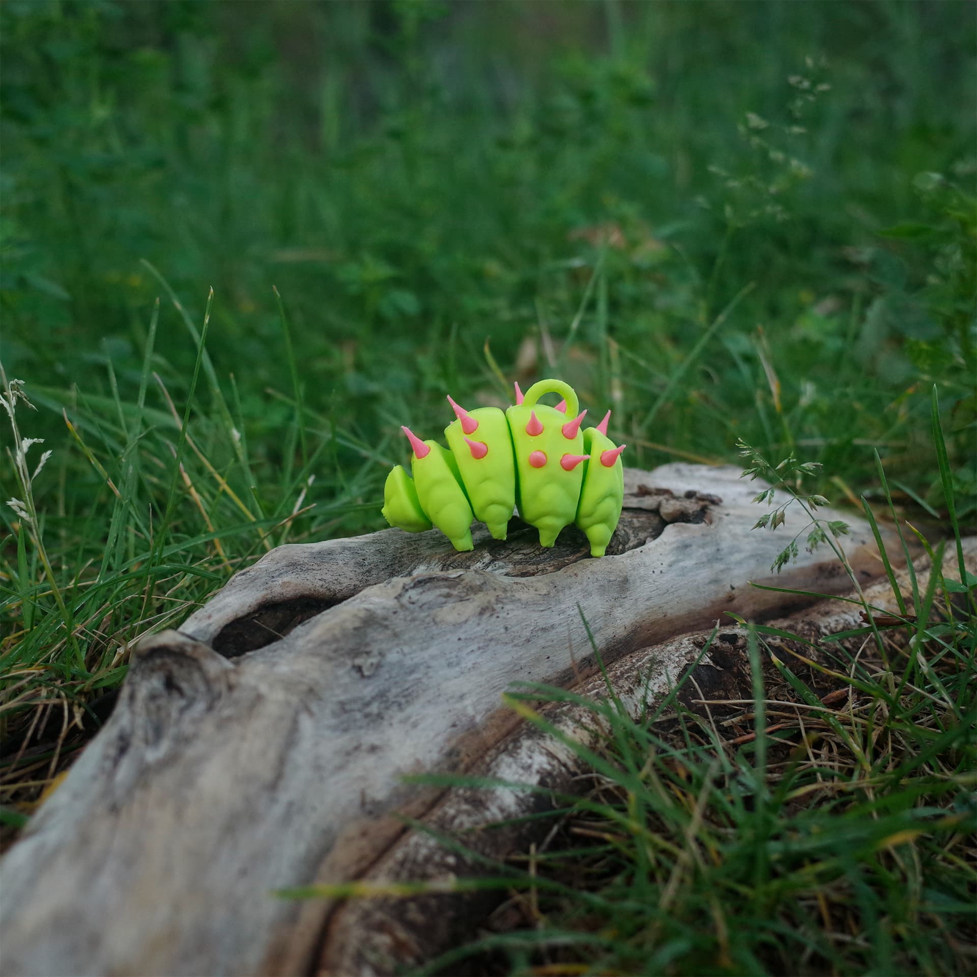 Side view of a spiked 3D printed tardigrade charm, standing on driftwood in a forest-like setting.
