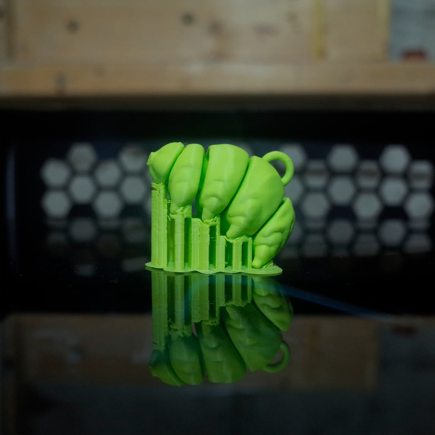 Side view of a green 3D printed tardigrade in its support structure, displayed on a reflective print bed.