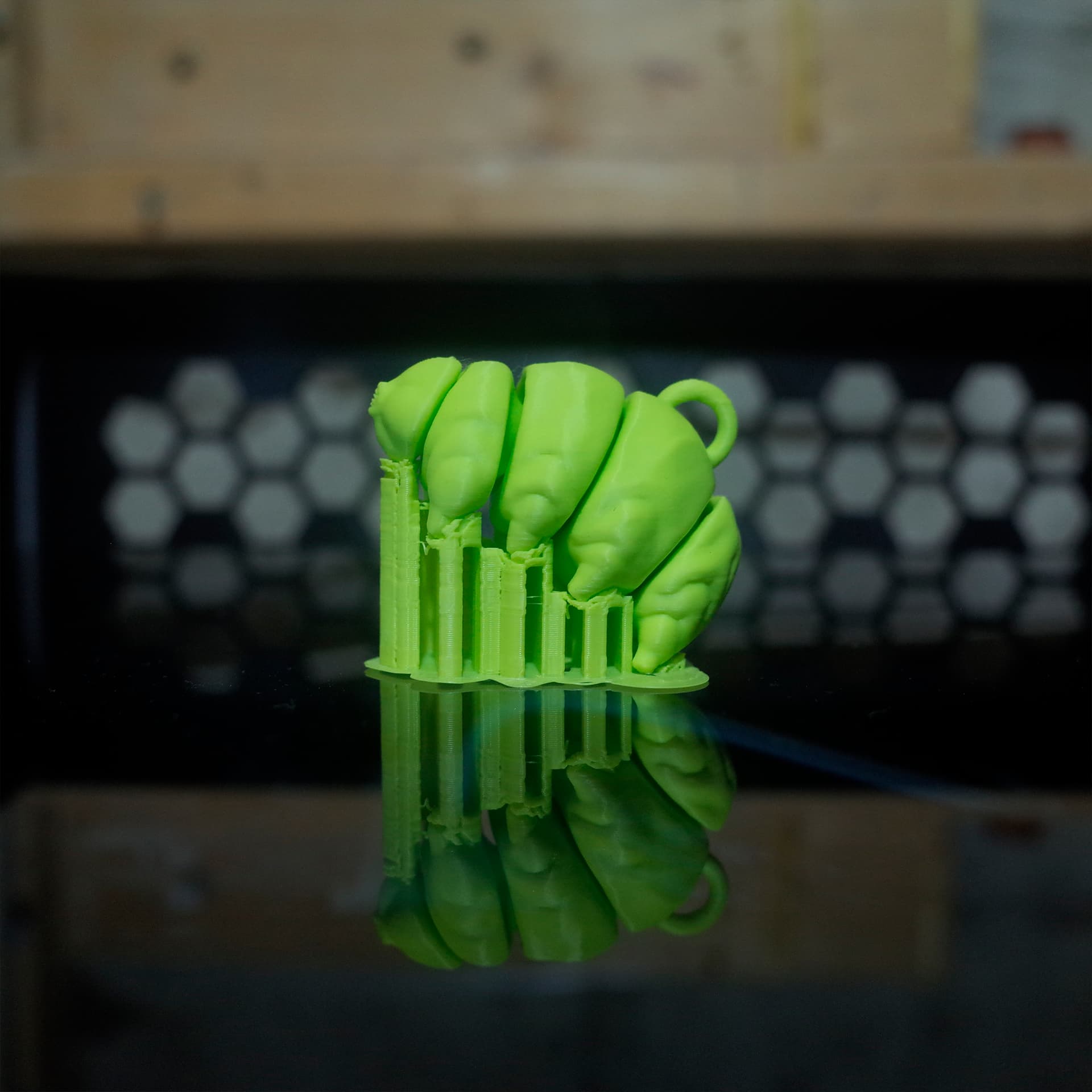 Side view of a green 3D printed tardigrade in its support structure, displayed on a reflective print bed.