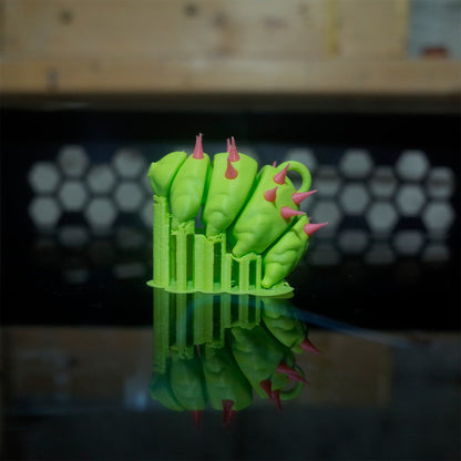 A punk-style green tardigrade toy with pink spikes, on a mirrored printer base.