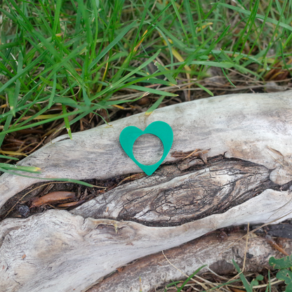 A vivid green heart-shaped 3D printed ring resting on a rustic log.